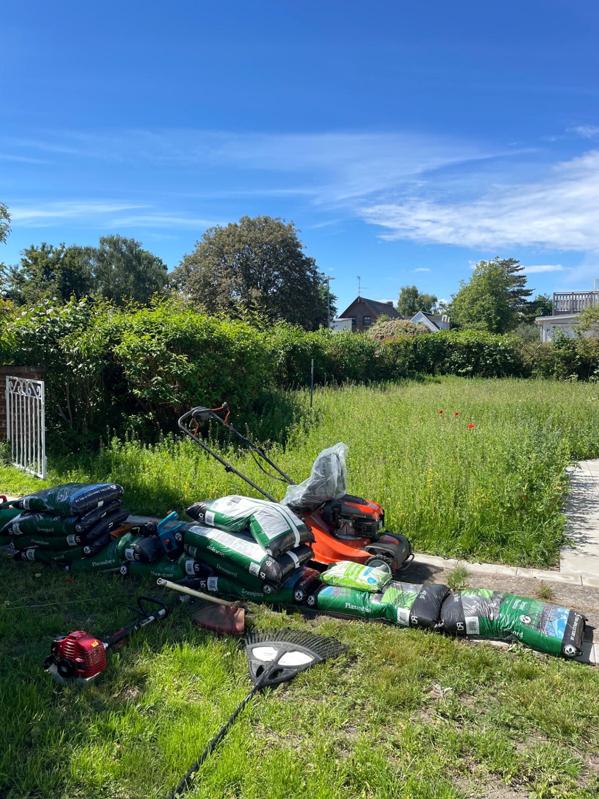 Gräsklippare, trimmer och säckar med dressjord på plats i trädgården